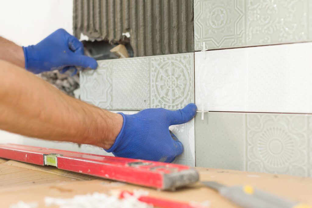 Closeup of tiler hand laying ceramic tile on wall in kitchen, renovation, repair, construction.