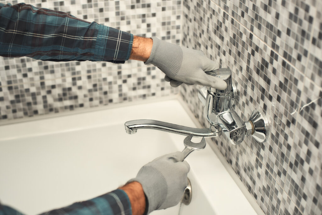 Close up of male hands holding a wrench, while fixing faucet in bathroom. Horizontal shot